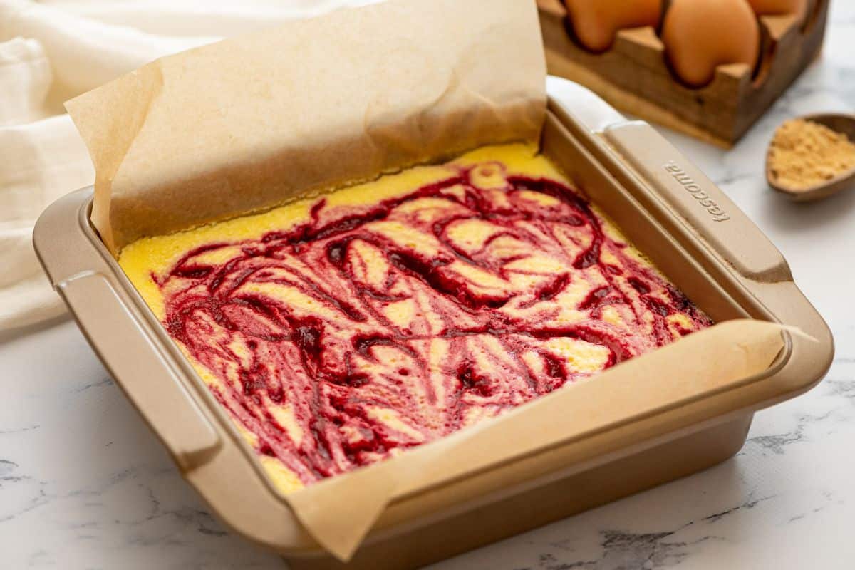Swirled cheesecake bars in parchment lined baking dish.