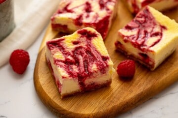 Sliced cheesecake bars on wooden cutting board revealing the raspberry swirl throughout the cheesecake batter.