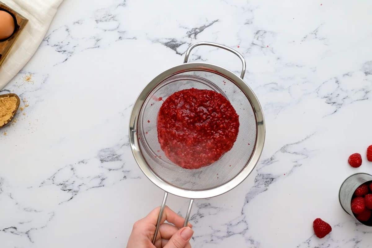 Fine mesh strainer showing removing seeds from raspberry puree.
