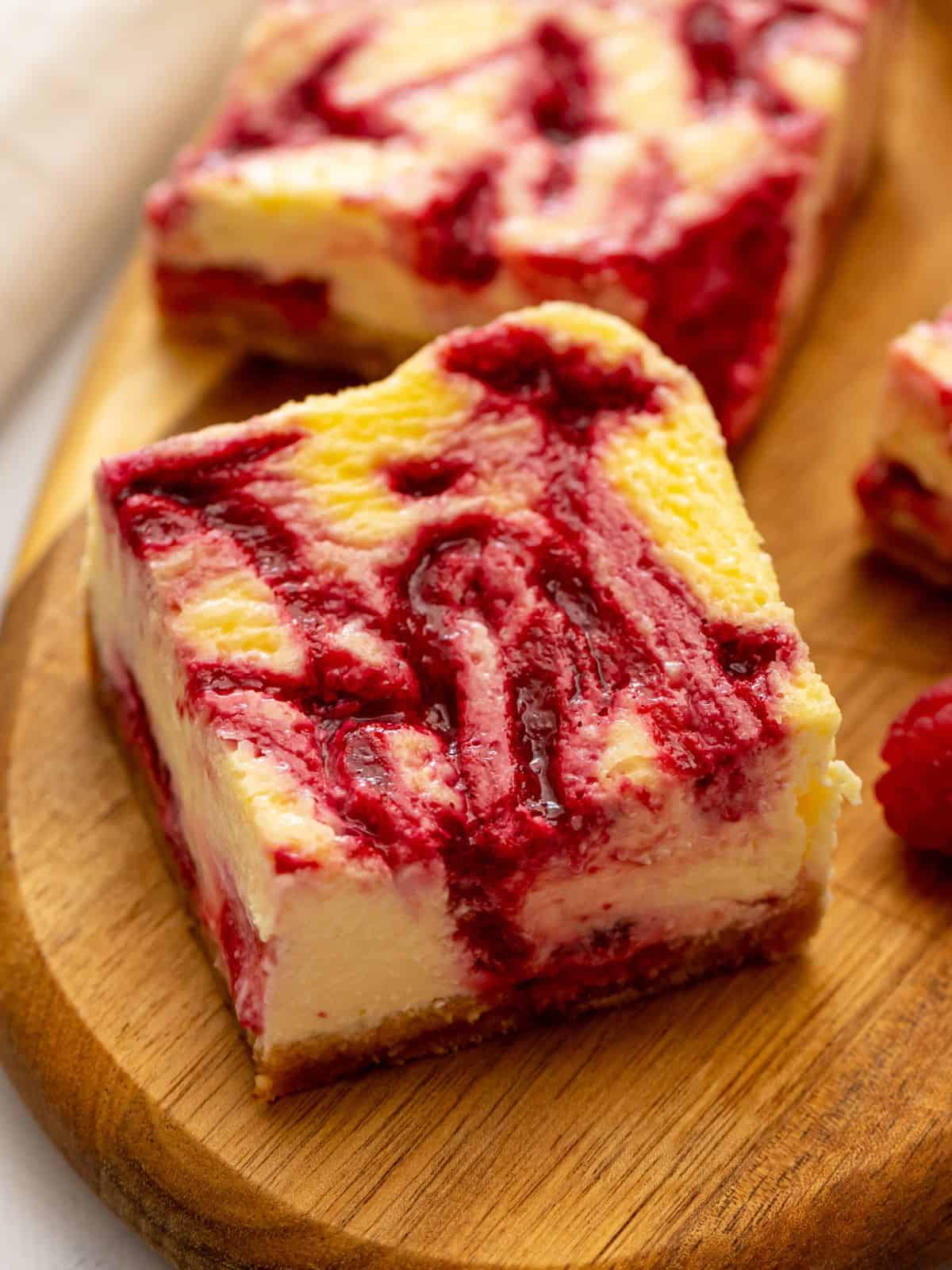Sliced cheesecake bars on wooden cutting board revealing the raspberry swirl throughout the cheesecake batter.