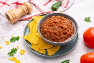 Homemade salsa in gray bowl next to tortilla chips and fresh tomatoes.