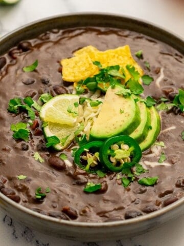 Bowl of Pressure Cooked Black Bean soup topped with cilantro, avocado, and sliced jalapeno.