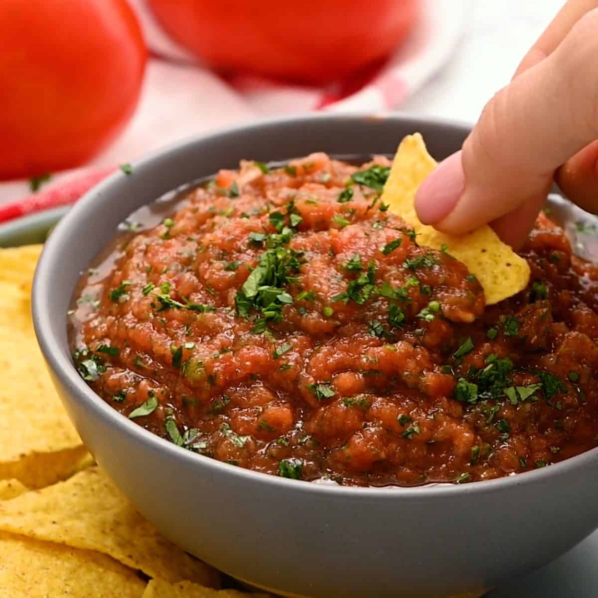 Favorite Super Bowl Recipes Chip scooping out chunky blender tomato salsa from grey bowl.