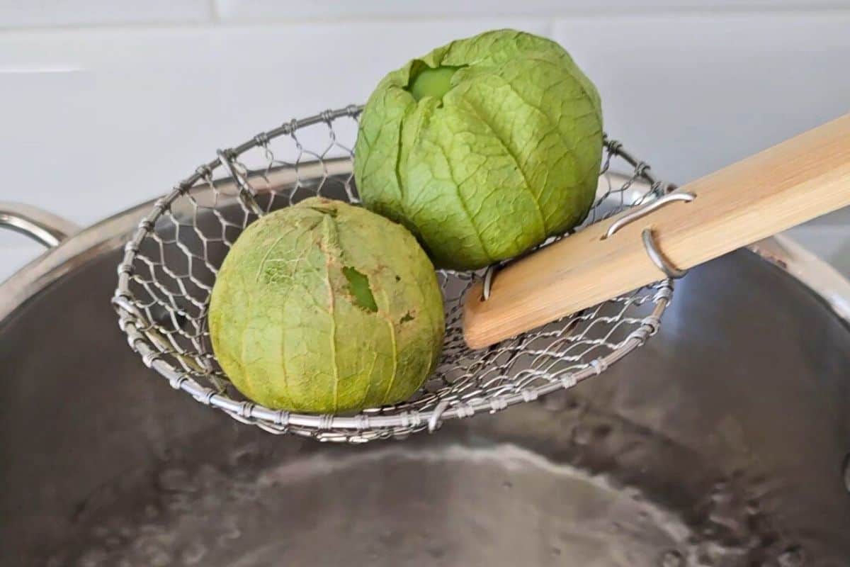 Spider spoon placing tomatillos into boiling hot water.