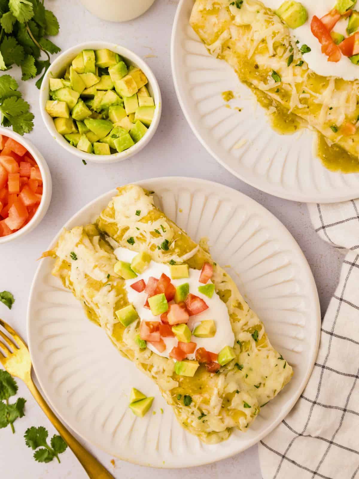 Green Salsa Verde Enchiladas made with chicken on white plate topped with diced avocado and diced tomatoes.