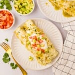 Salsa Verde Chicken Enchiladas on white plate topped with diced avocado and diced tomatoes.