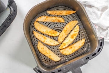 Seasoned potato wedges in a single layer in the air fryer before air frying.