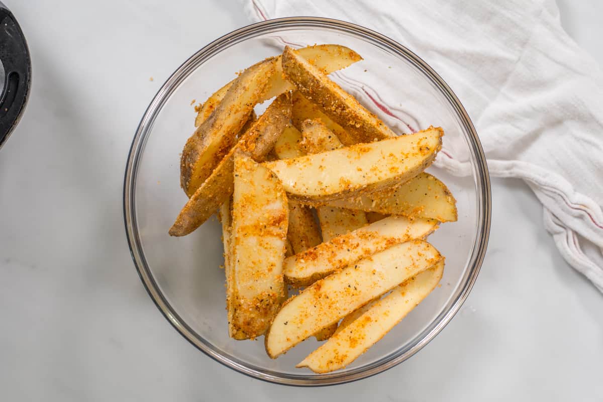 Mixing bowl with potato wedges coated in flour, parmesan, and seasonings.