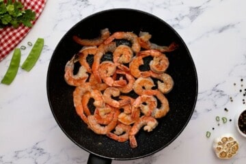 Sauteed shrimp in large saute pan next to garlic and green onions.