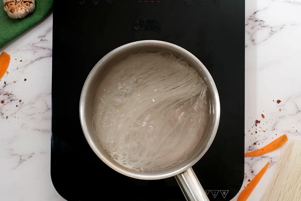 Rice vermicelli cooking in boiling water in medium saucepan.