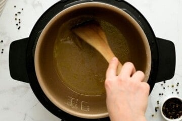 Wooden spoon scraping up browned bits on bottom of inner pot after searing chicken thighs.