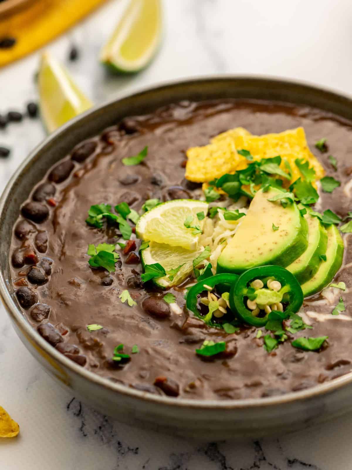 Bowl of Instant Pot Black Bean soup topped with cilantro, avocado, and sliced jalapeno.