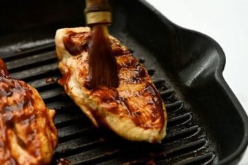 Grilled Chicken Breasts on grill plate being brushed with barbecue sauce.