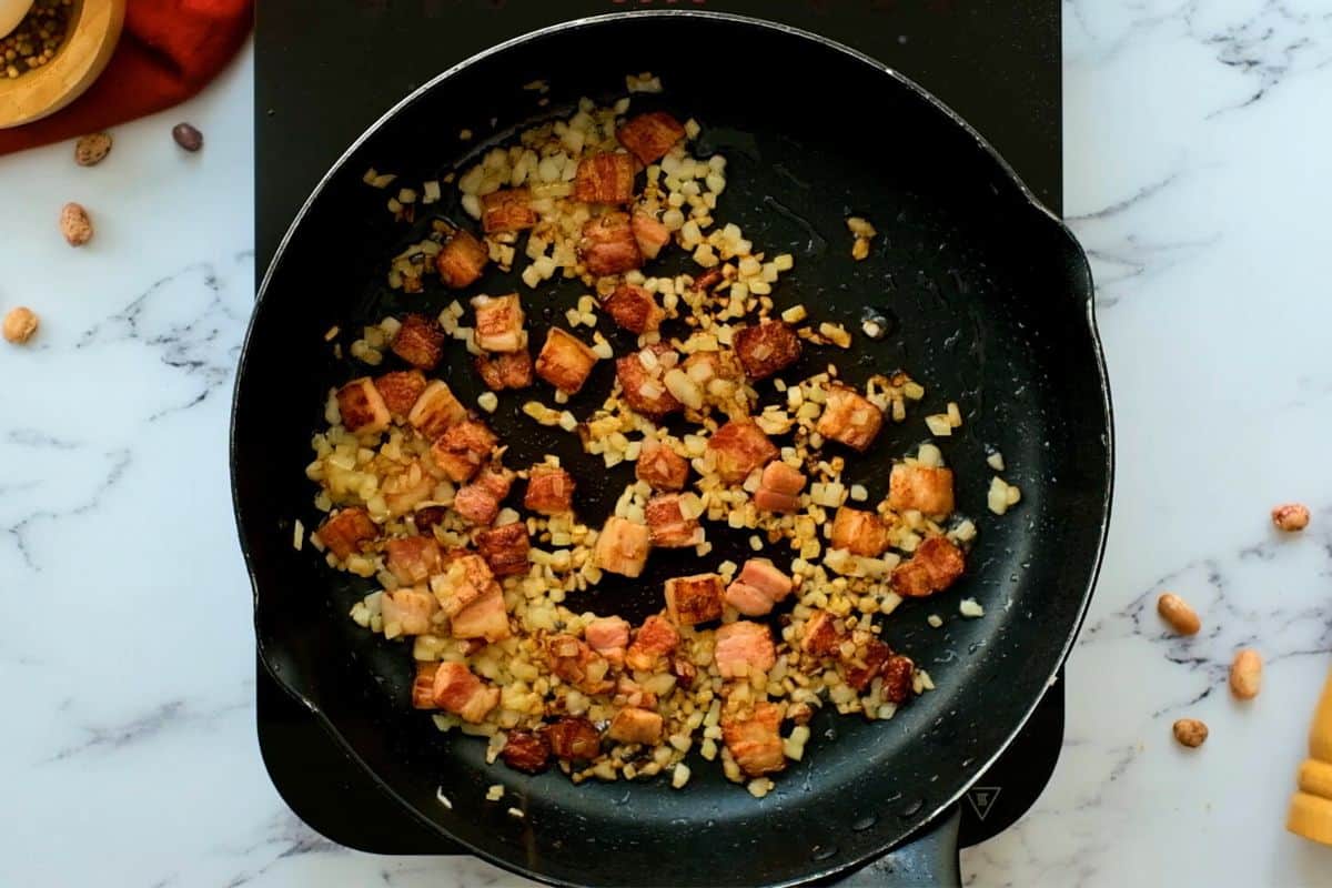 Cubed bacon and minced onion together in large sauté pan after bacon has been rendered and cooked.