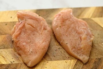 Seasoned chicken breasts on wooden cutting board.