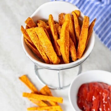 White container with crispy sweet potato fries next to ketchup.