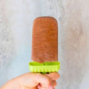 Child's hand holding homemade Fudgesicle with green handle.