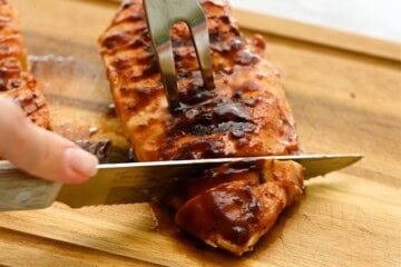BBQ Chicken Breasts on wooden cutting board being cut into thin strips.