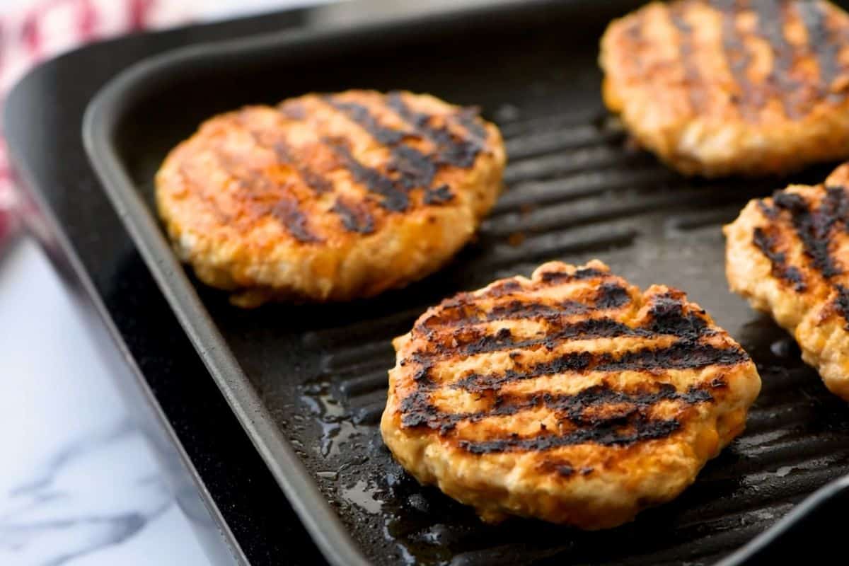 Four chicken burgers on grill plate.