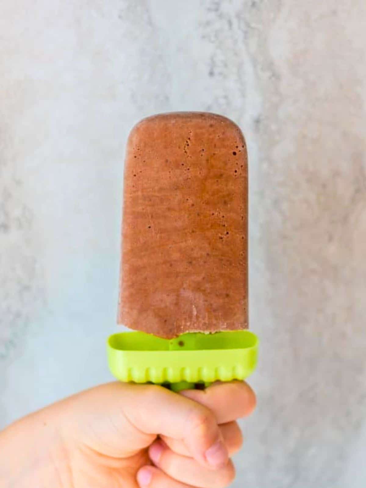 Child's hand holding homemade Fudgesicle with green handle.