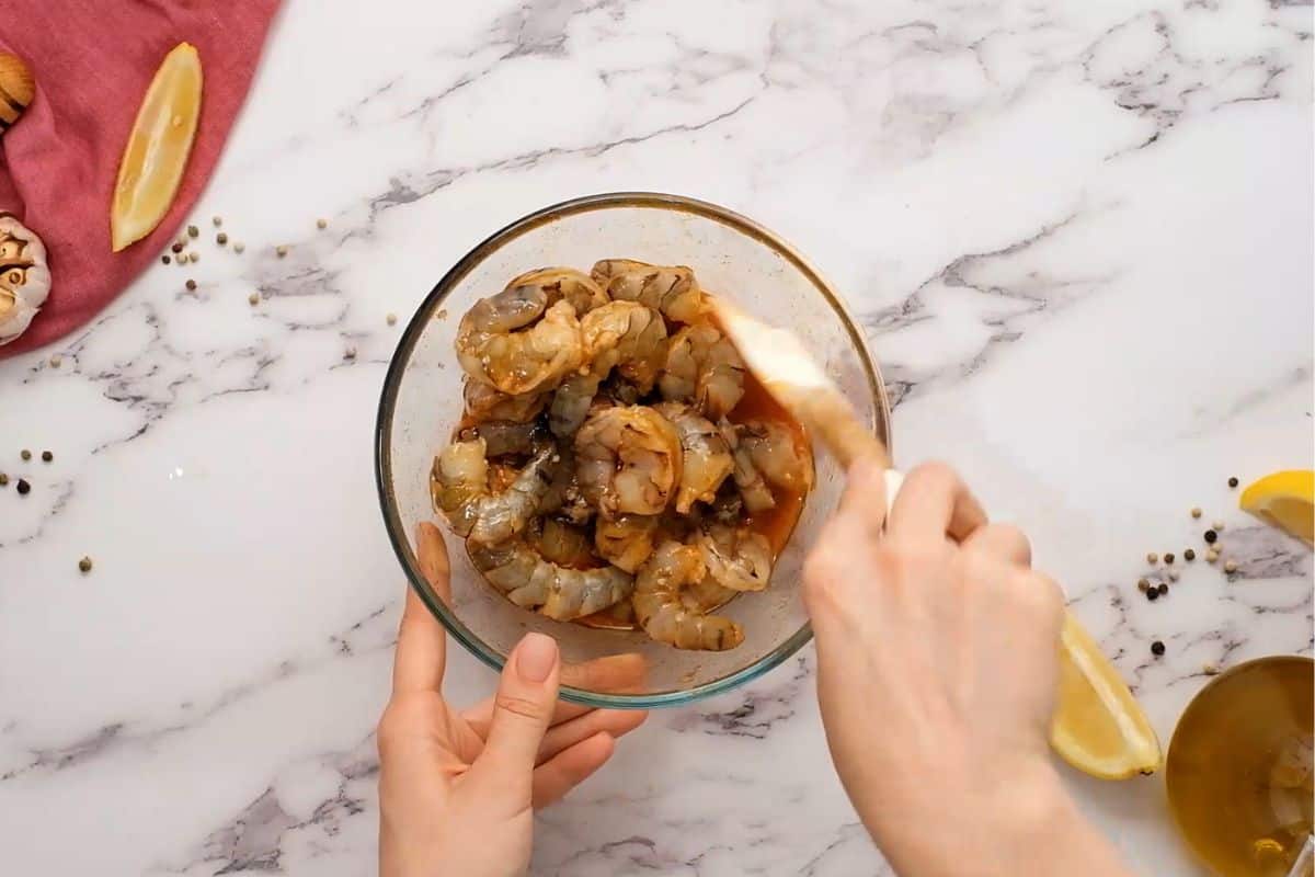 Raw shrimp being tossed in honey lemon marinade with garlic.