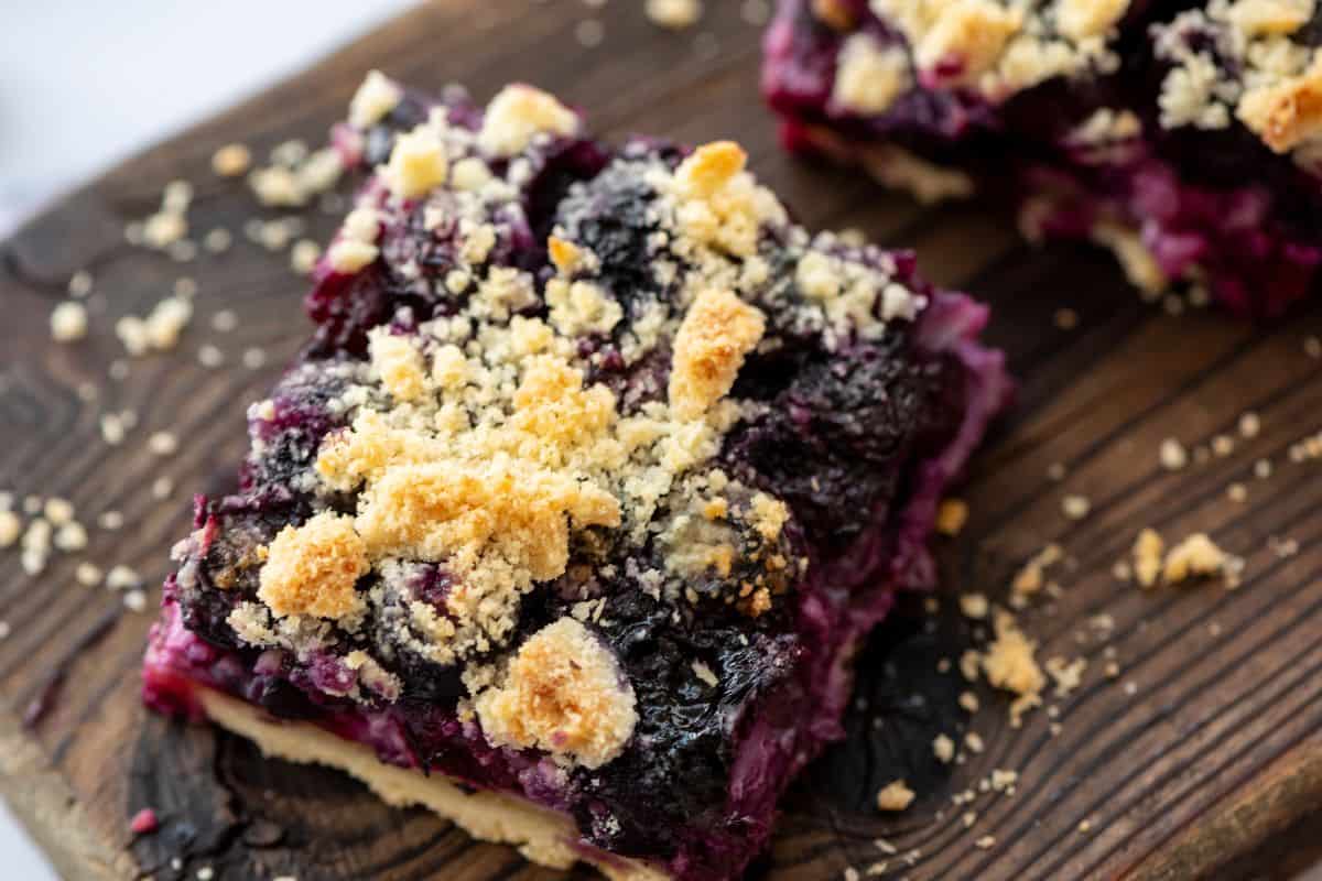 Sliced blueberry pie bars on wooden cutting board showing shortbread crumble.