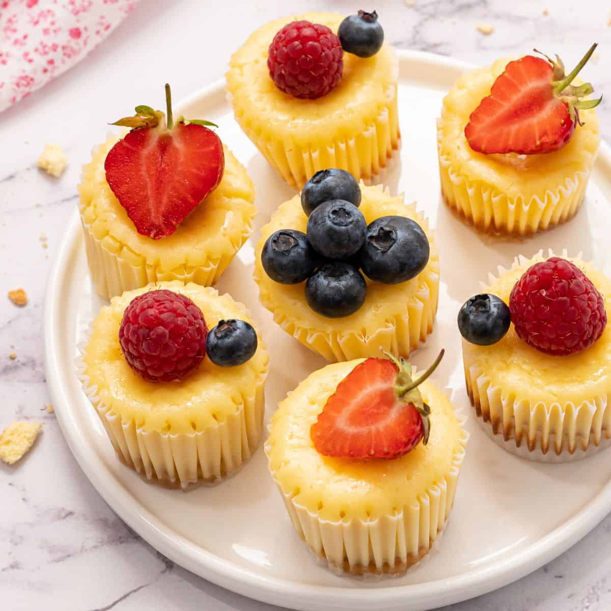 Desserts for Super Bowl Party Mini cheesecakes on white plate topped with fresh fruit.