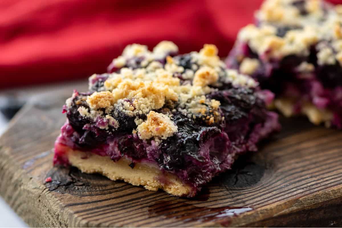 Sliced blueberry bars on wooden cutting board showing shortbread crumble.