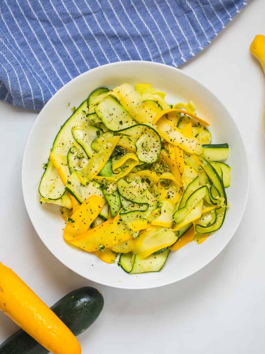 Ribbons of zucchini and squash in a white bowl topped with parsley.