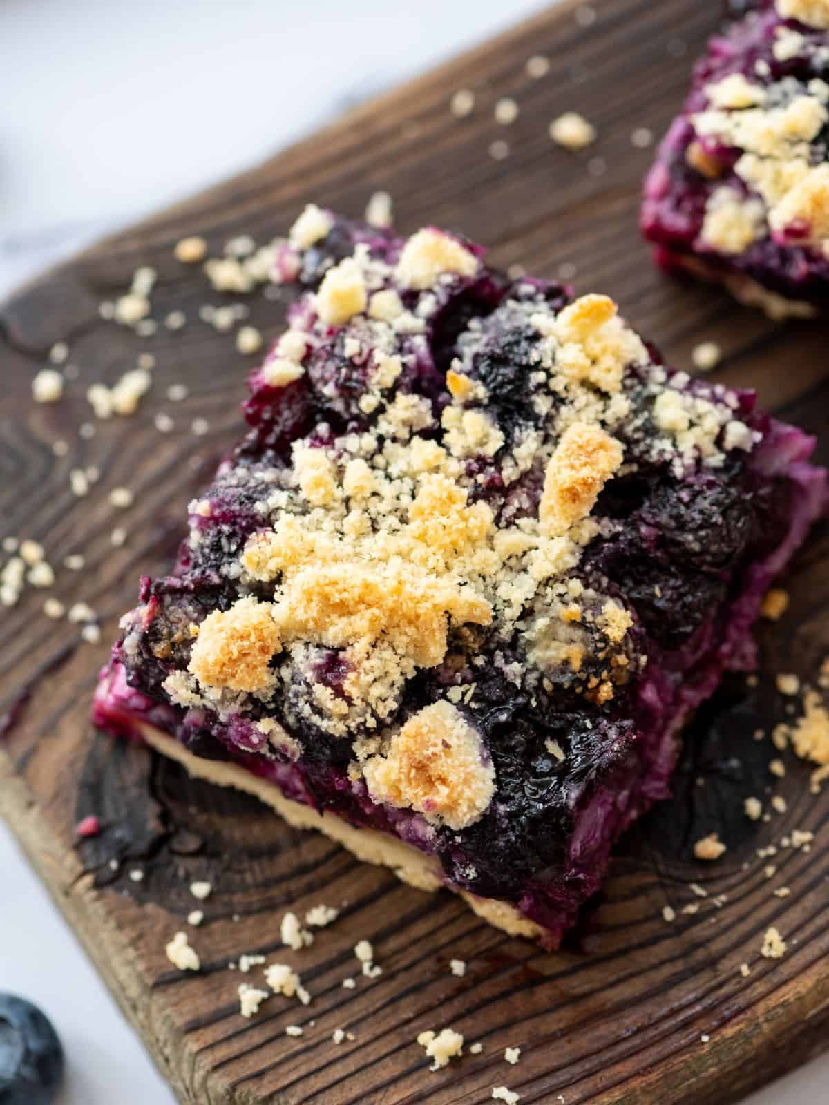 Sliced blueberry pie bars on wooden cutting board showing shortbread crumble.