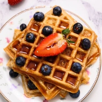 3 whole wheat waffles on white plate topped with berries and maple syrup.