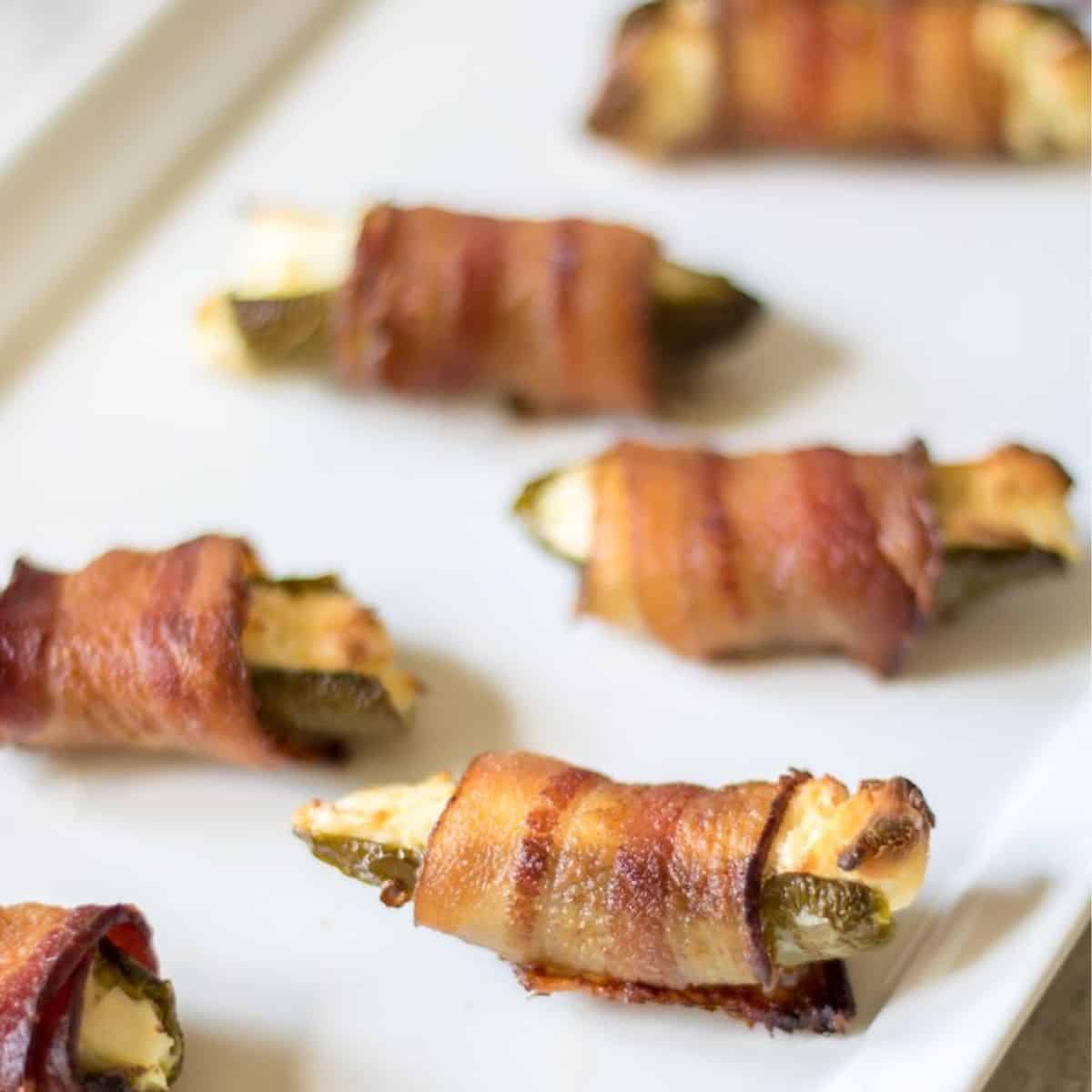 Game Day Recipe Ideas Bacon-Wrapped Jalapeno Poppers on white platter after being baked and toothpicks removed.