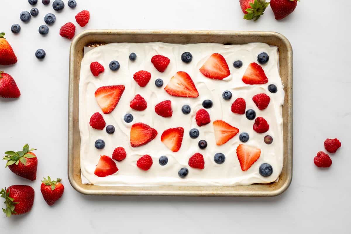 Yogurt spread on baking sheet that has been lined with parchment paper topped with strawberries, raspberries, and blueberries.