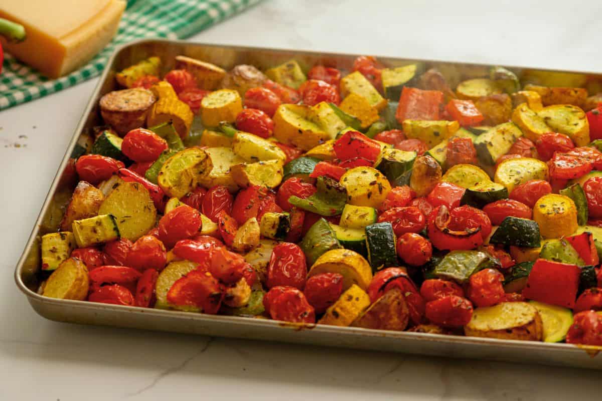 Roasted potatoes, squash, and tomatoes on rimmed sheet pan topped with parmesan cheese.