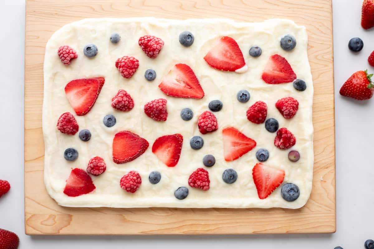 Frozen Yogurt Bark with Berries on wooden cutting board with fresh berries on around the yogurt.