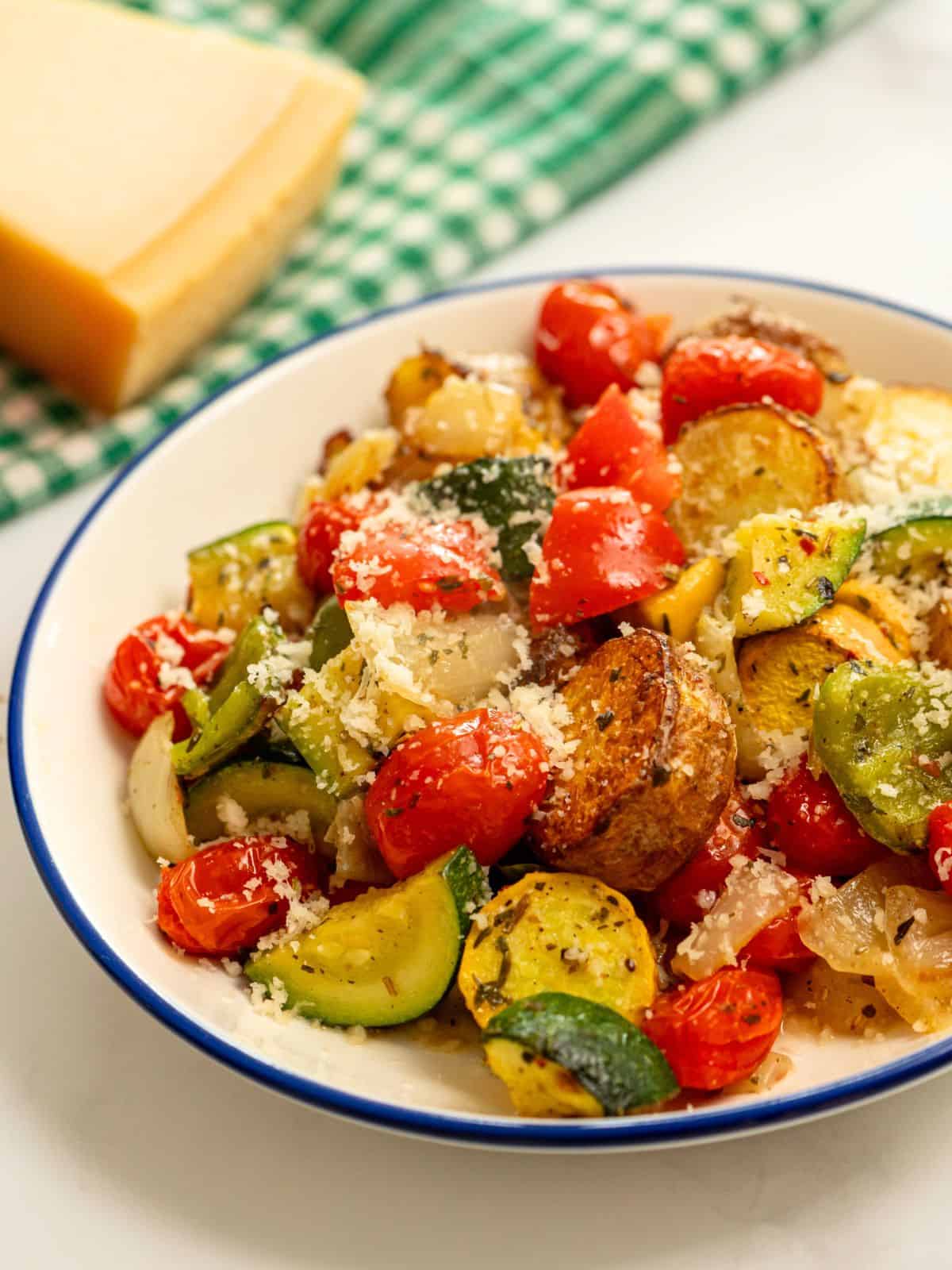 Roasted Italian Vegetables dished up in blue and white bowl topped with parmesan cheese.
