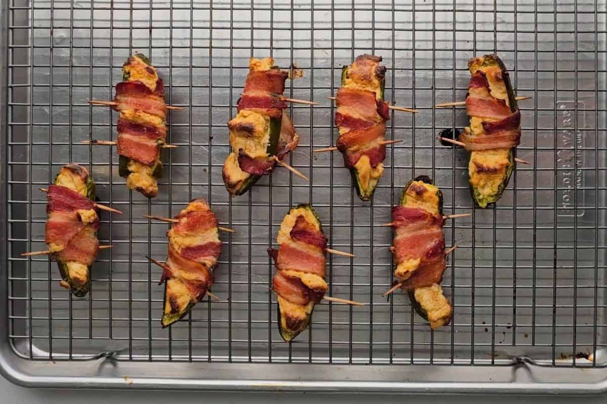 Jalapeno Poppers on baking sheet wrapped in bacon after being baked.