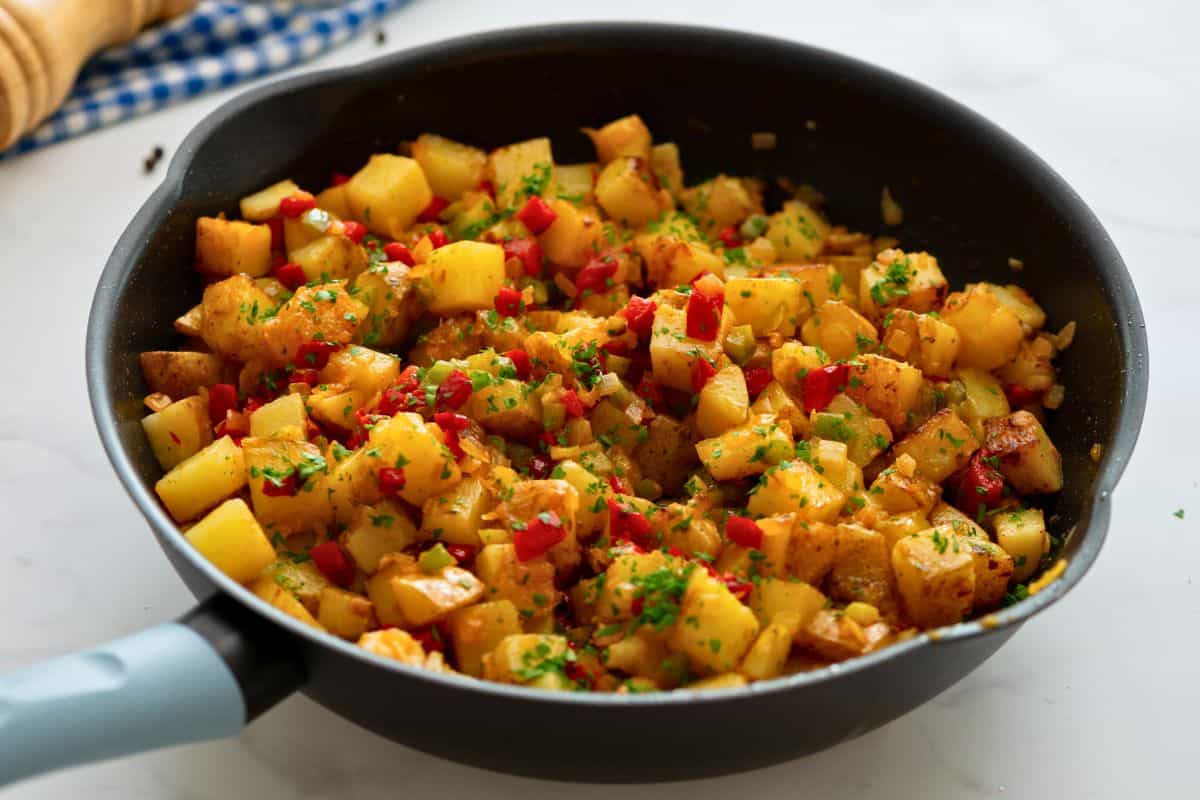 Pan-fried potatoes with peppers and onions topped with fresh parsley in large saute pan.