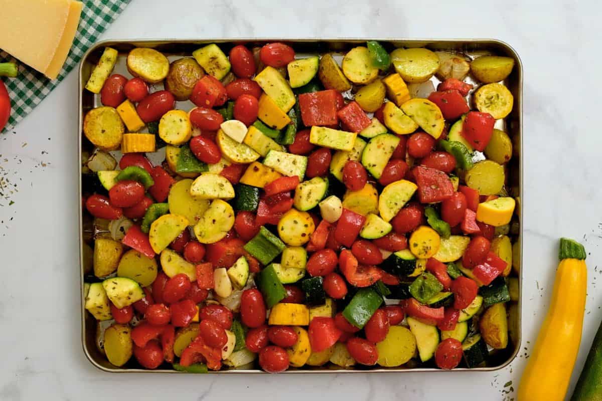 Italian seasoned peppers, squash, and potatoes on large rimmed sheet pan with tomatoes.