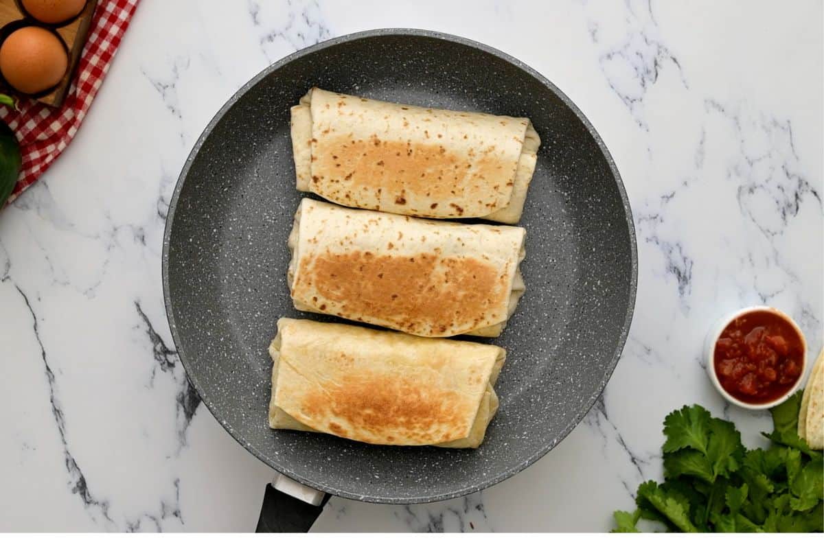 Toasted breakfast burritos in dry skillet.