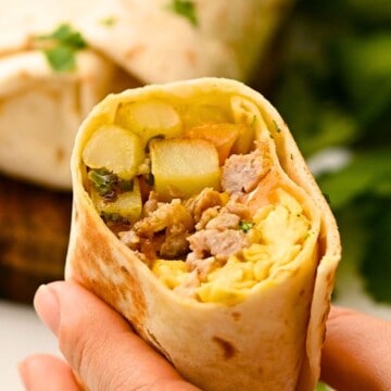 Loaded breakfast burrito cut in half to reveal eggs, sausage, and potatoes on inside.