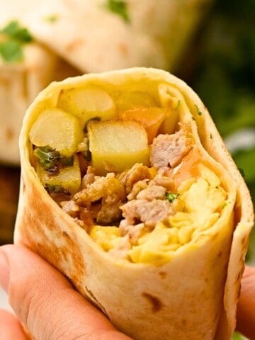 Loaded breakfast burrito cut in half to reveal eggs, sausage, and potatoes on inside.