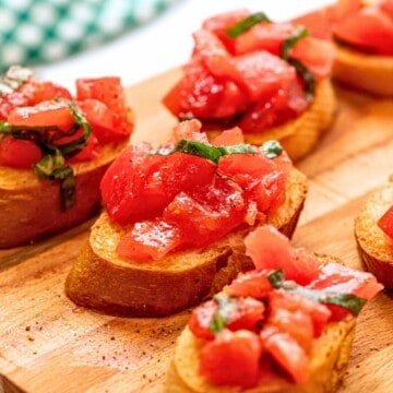 Bruschetta on wooden cutting board topped with tomatoes and basil.