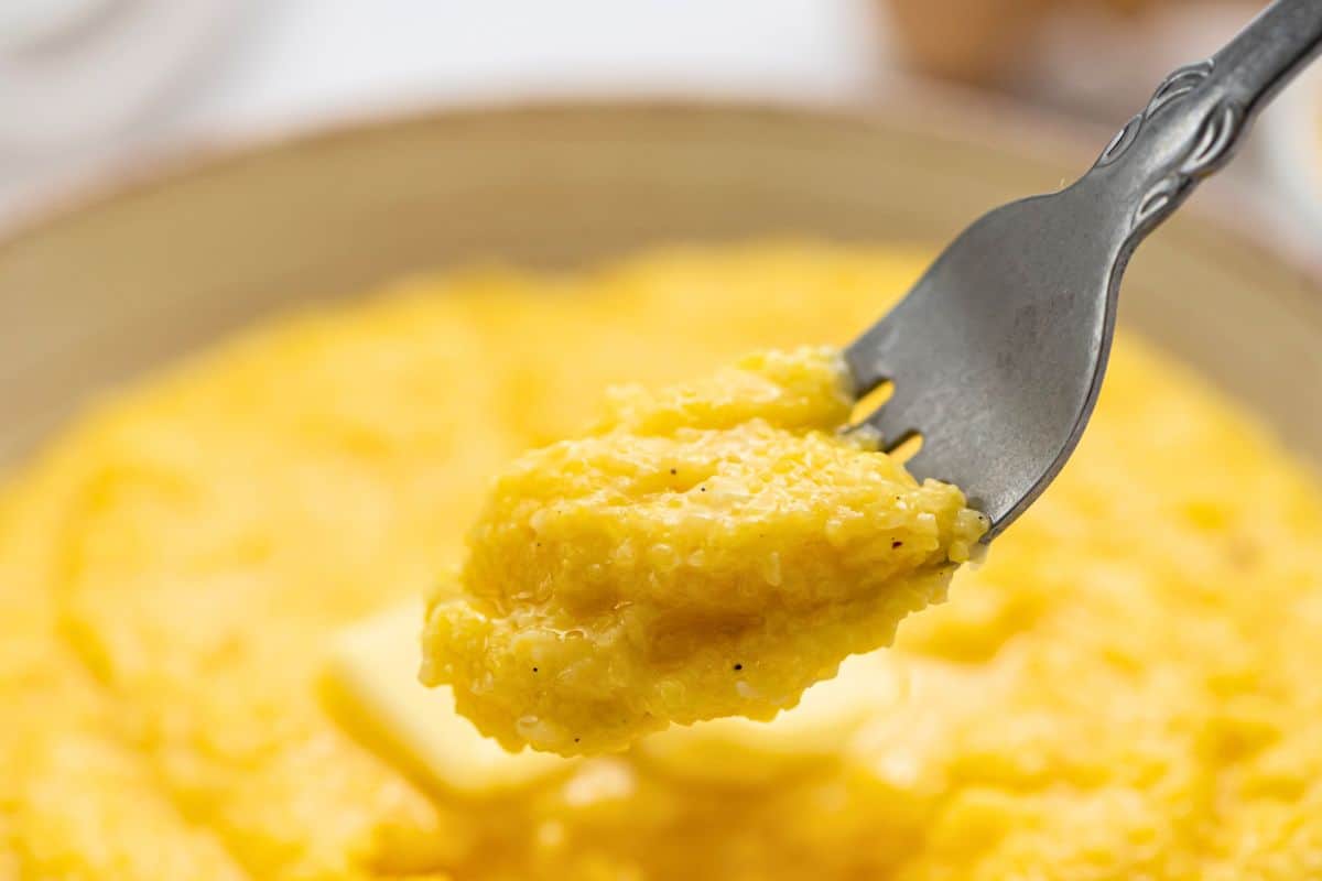 Fork full of creamy cheese grits being dished out of a bowl of grits.