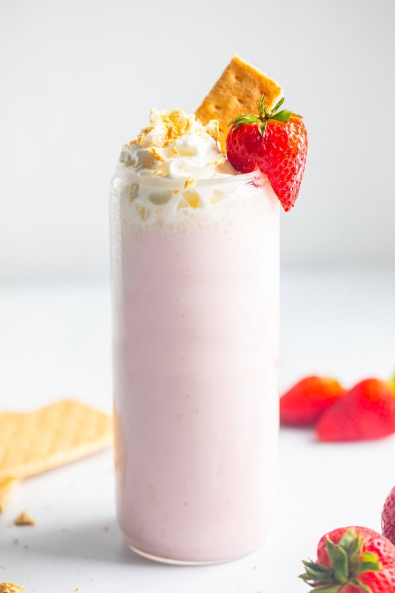 Cottage Cheese Smoothie made with cottage cheese and strawberries topped with whipped cream with crushed graham crackers on top and fresh strawberries in background.