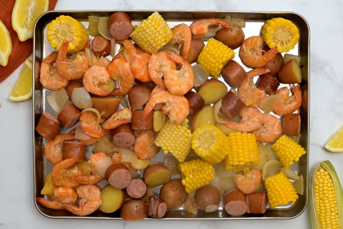 Seafood shrimp boil spread out on rimmed baking sheet pan after cooking liquid was drained off.