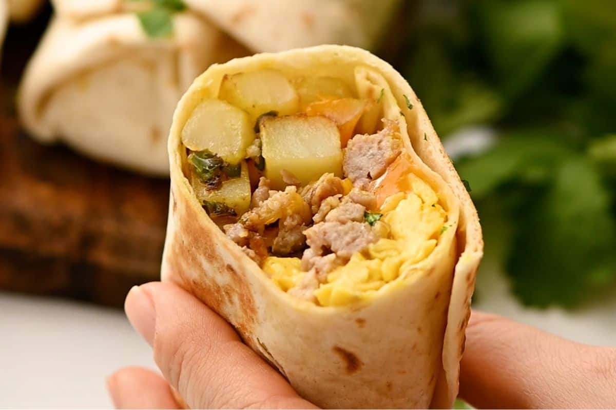 Loaded breakfast burrito cut in half to reveal eggs, sausage, and potatoes on inside.