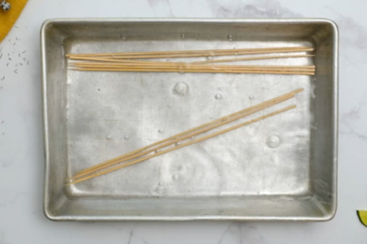 Wooden skewers being soaked in a metal dish.