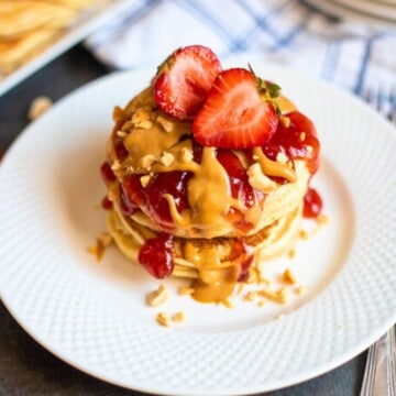 Stack of peanut butter pancakes topped with strawberry sauce and peanut butter syrup.