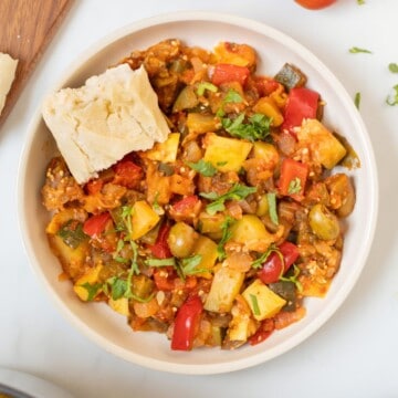 Thick Classic Ratatouille dished up in bowl topped with basil and served with crusty bread on the side.